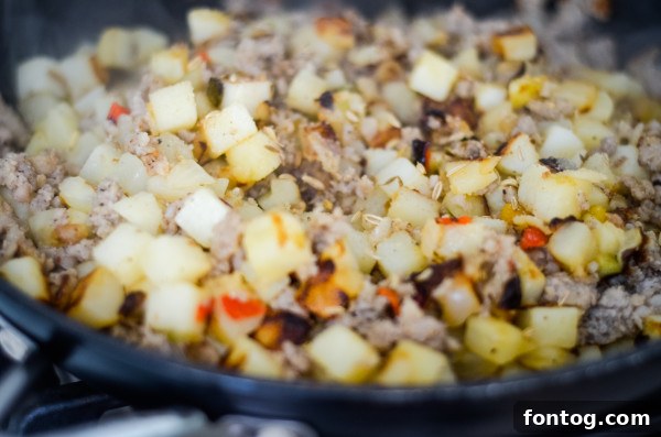 Savory Sausage, Egg, and Cheese Breakfast Hash 3 Close-up of golden brown potatoes and sausage cooking in a skillet