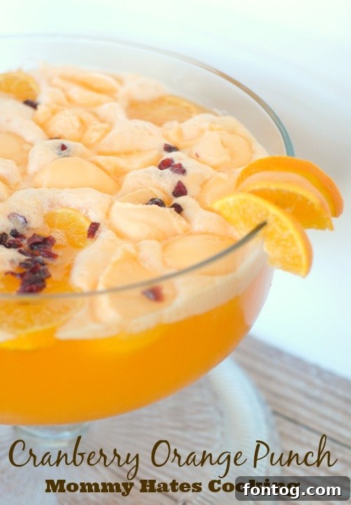 Vibrant Cranberry Orange Punch in a beautiful glass dispenser, garnished with fresh orange slices and cranberries.