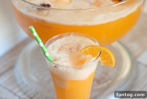 A full punch bowl and several glasses of Cranberry Orange Punch set on a festive table.