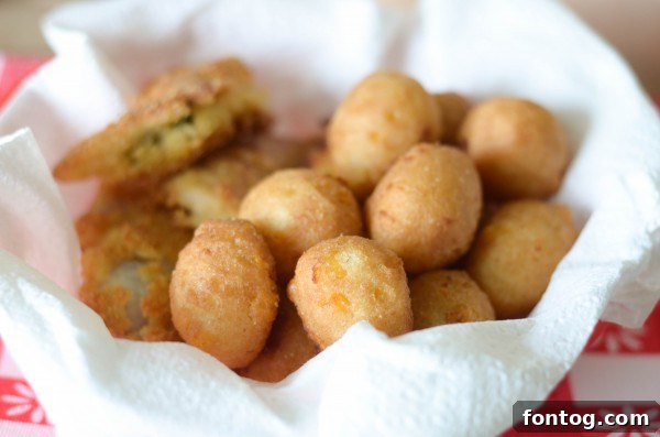Close-up shot of perfectly golden and crispy catfish nuggets and sweet corn hush puppies on a festive red and white checkered tablecloth.