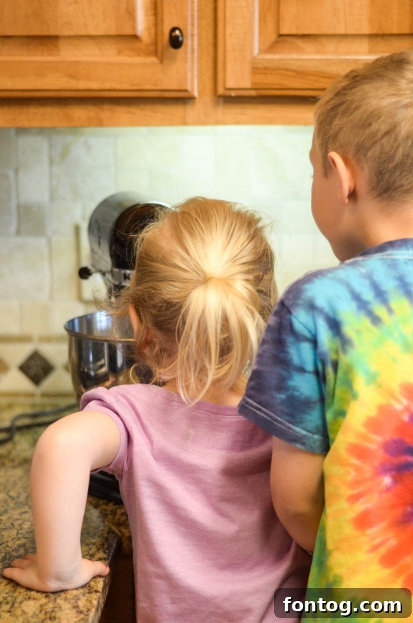 Fresh Bloom Cupcakes 7 A young boy's hand gently guiding his younger sister's hand while pouring ingredients into a mixing bowl, showcasing sibling cooperation during baking.