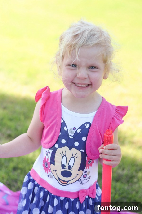 Little girl joyfully playing with bubbles in a Minnie Mouse dress during an outdoor picnic. #MinnieMouseDress #KidsActivities