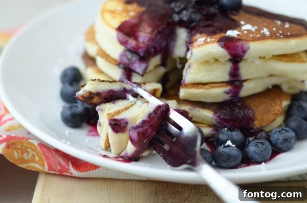 Blueberry sauce being poured over pancakes