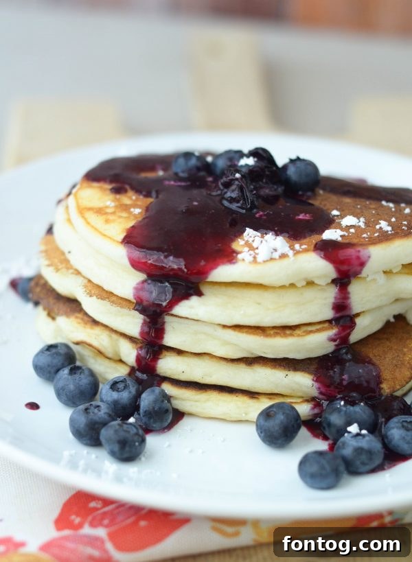 A serving of buttermilk pancakes with a generous pour of blueberry sauce and fresh blueberries