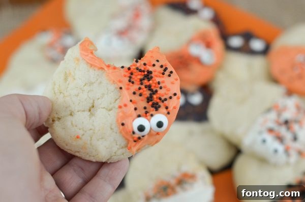Spooky Sugar Cookies - Hand holding a freshly decorated Halloween sugar cookie with orange candy melt and candy eyeballs.