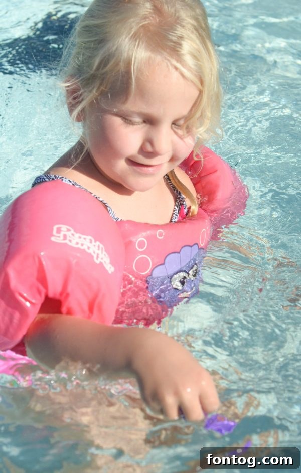 A child's hands reaching for a Lil' Fishy toy underwater in a swimming pool