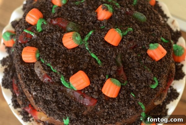 Close-up of a Pumpkin Patch Cake featuring crushed cookies, gummy worms, and candy pumpkins.