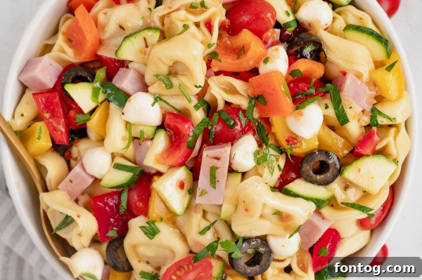 Pouring Italian dressing over the tortellini and vegetables in a bowl