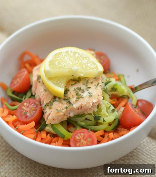 A vibrant Green Giant Veggie Spiral bowl featuring grilled salmon, fresh tomatoes, lemon, and parsley atop a mix of carrot and zucchini spirals, ready for a delicious and healthy meal.