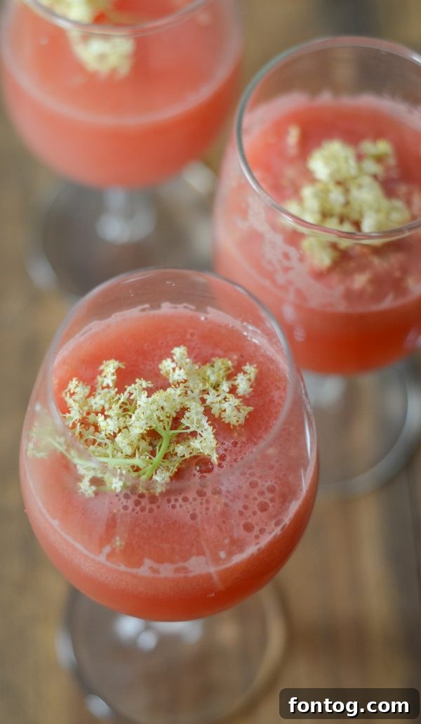 Watermelon Pineapple Punch with Elderflower in a tall glass, garnished with fruit slices and blossoms