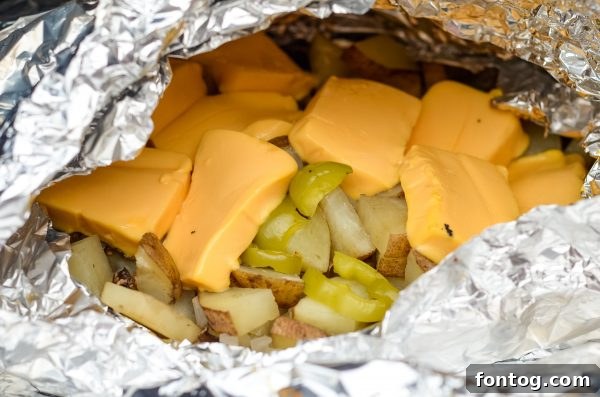 Your New Favorite Cheesy Grilled Potatoes 4 hands preparing a foil packet with diced potatoes, bell pepper, mushrooms, and onion, seasoned with salt, pepper, and garlic powder