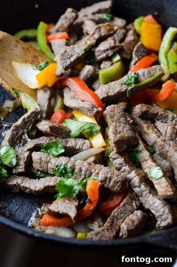 skillet of cooked beef fajita meat with a wooden spoon