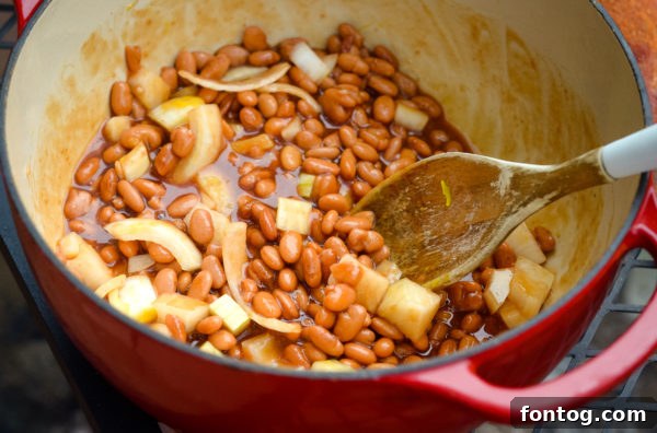 Close-up of Campfire Beans being stirred in a cast iron skillet over a fire, showcasing the rich texture and vibrant ingredients.
