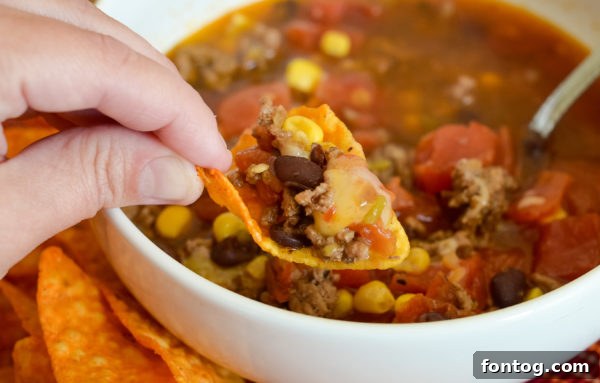 A bowl of Ninja Foodi Beef Taco Soup with Hatch Chiles, garnished with cheese and a spoon, ready to be enjoyed.