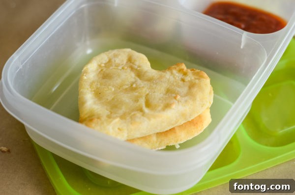 An open multi-compartment lunch box filled with pizza kit ingredients and a fruit