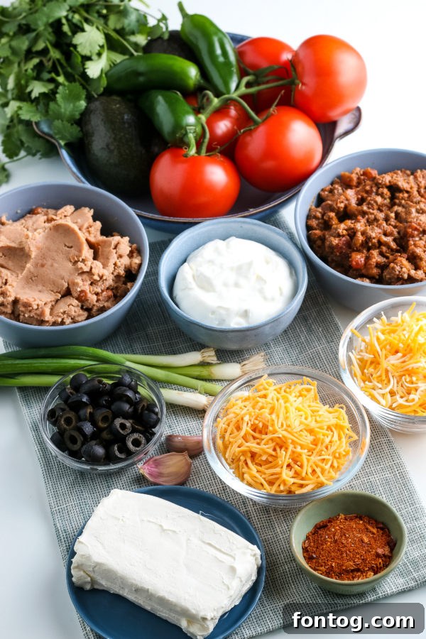 Ingredients laid out for making layered taco dip, including ground beef, seasoning, and various fresh toppings
