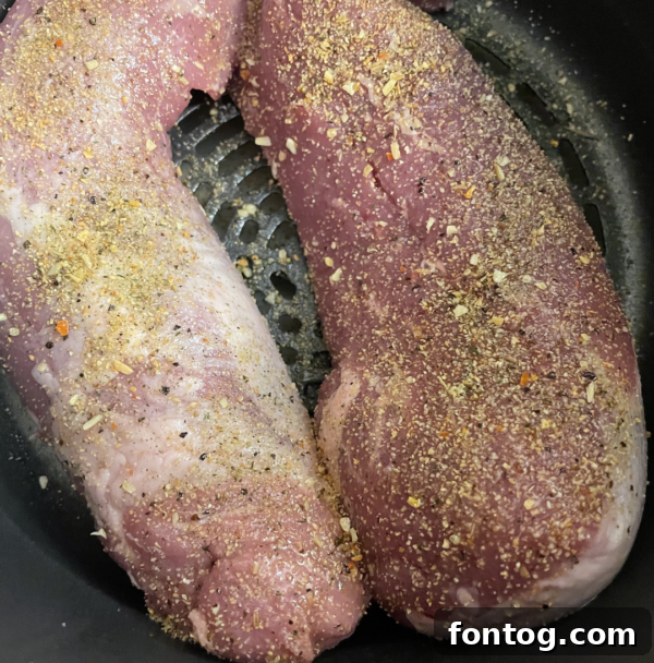 The cooking process of pork tenderloin in an air fryer basket, showing seasoning and placement.