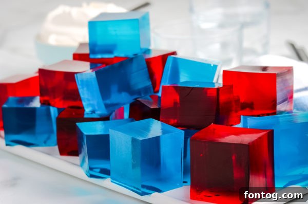 A serving platter filled with ready-to-eat Patriotic Jello Jigglers, garnished with fresh berries.