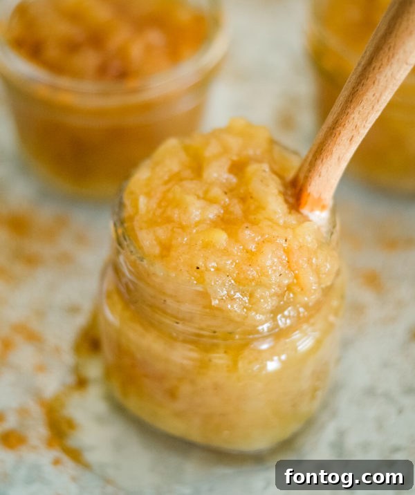 Freshly made Ninja Foodi applesauce in a serving bowl, garnished with cinnamon stick and whole apples in the background.