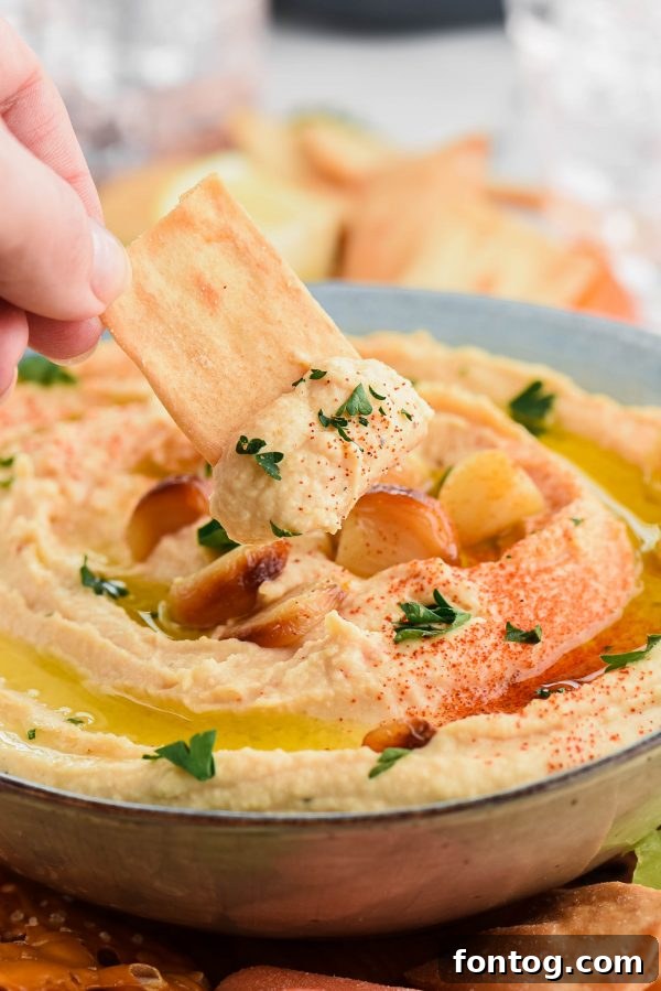 Freshly made roasted garlic hummus in a bowl, garnished with herbs and a drizzle of olive oil, ready for dipping with pita bread and vegetable sticks.
