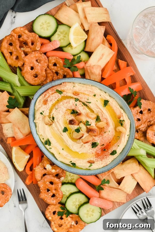 Roasted garlic hummus served on a platter with various fresh vegetable dippers and pita bread.