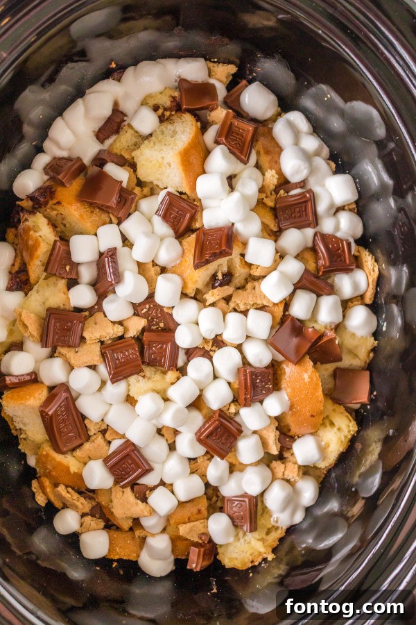 Slow Cooker S'mores French Toast Casserole, showing layers of bread and chocolate before adding marshmallows.