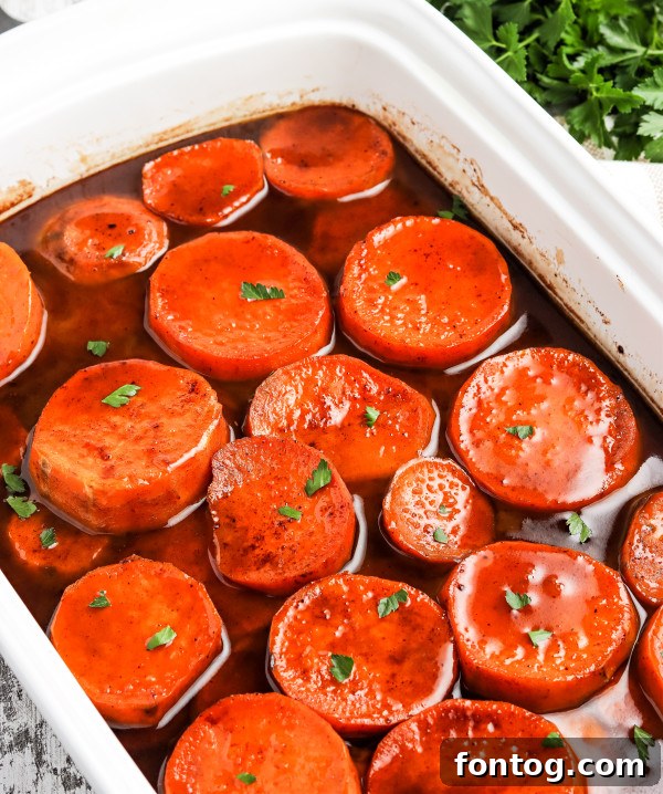 Baked candied yams bubbling in a clear glass baking dish, showing the glazed surface