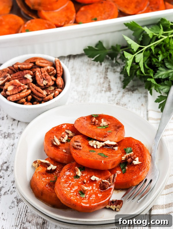 Finished baked candied yams in a white serving dish, garnished with fresh parsley and pecans