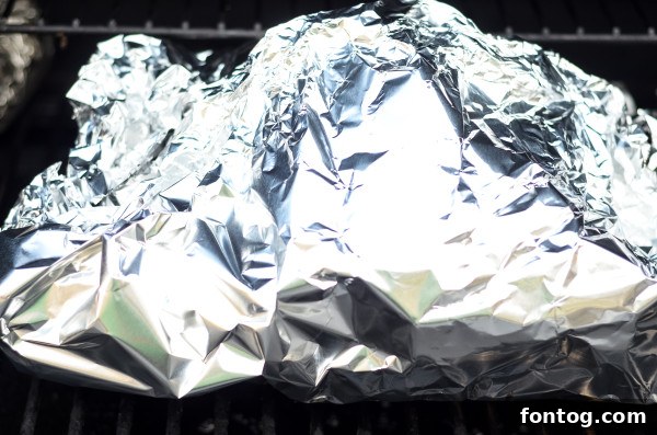 A large bone-in ham being placed carefully onto the grates of a pellet grill.