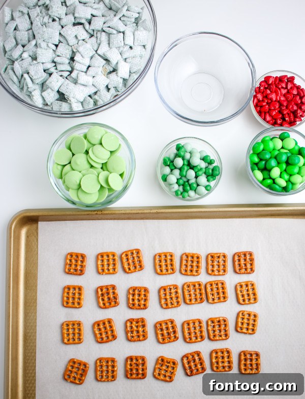 Ingredients for Grinch Pretzel Bites laid out: square pretzels, bright green candy melts, and red heart sprinkles.