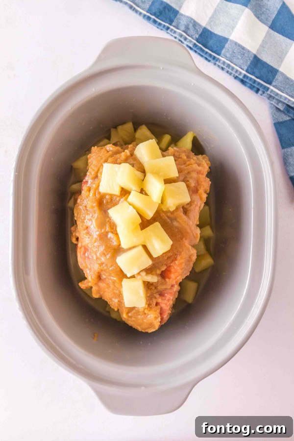 Pineapple tidbits and brown sugar glaze covering a ham in a slow cooker