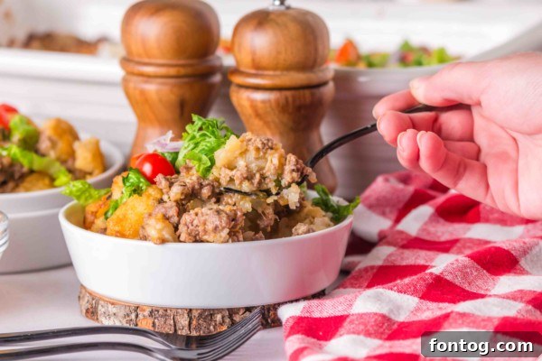 Serving of Big Mac Tater Tot Casserole with fresh lettuce and tomato toppings, ready to eat.