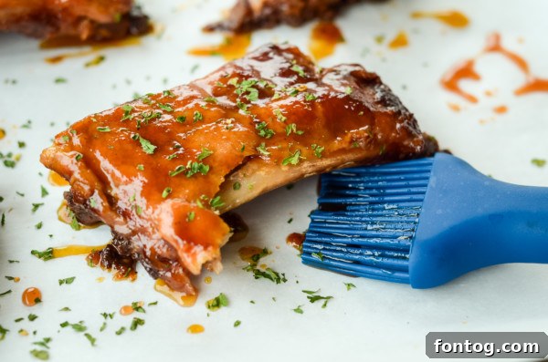 A hand brushing rich apple barbecue sauce onto slow cooker apple bbq ribs.