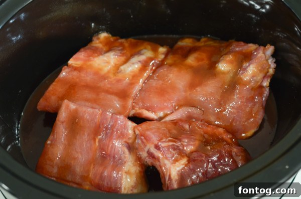Sections of baby back ribs neatly arranged in a slow cooker, ready for the sauce.