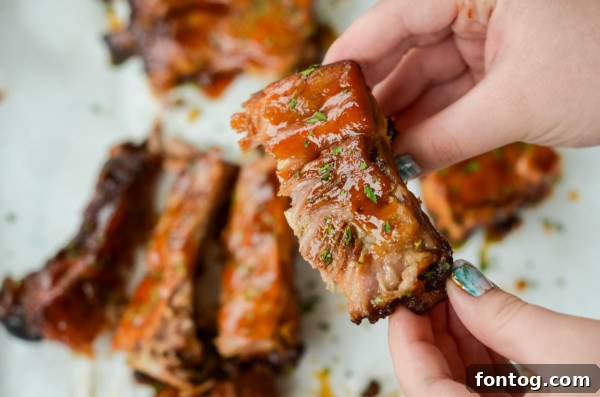 A person reaching for a piece of slow cooker baby back rib with apple barbecue sauce, ready to eat.