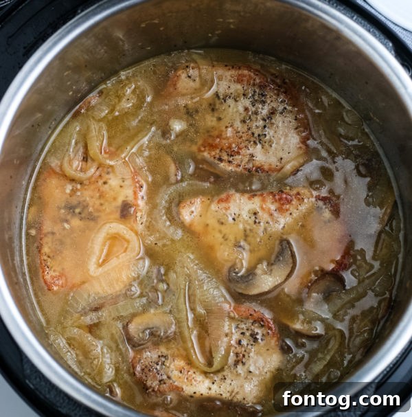 Pressure cooker with pork chops and gravy inside during cooking