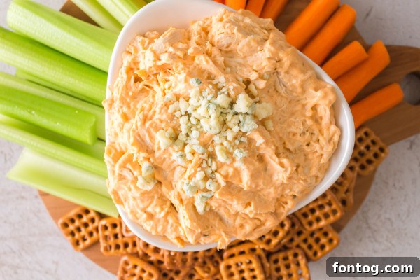 Spicy chicken dip served in a bowl with a colorful assortment of dippers, including tortilla chips, celery sticks, and carrot sticks.