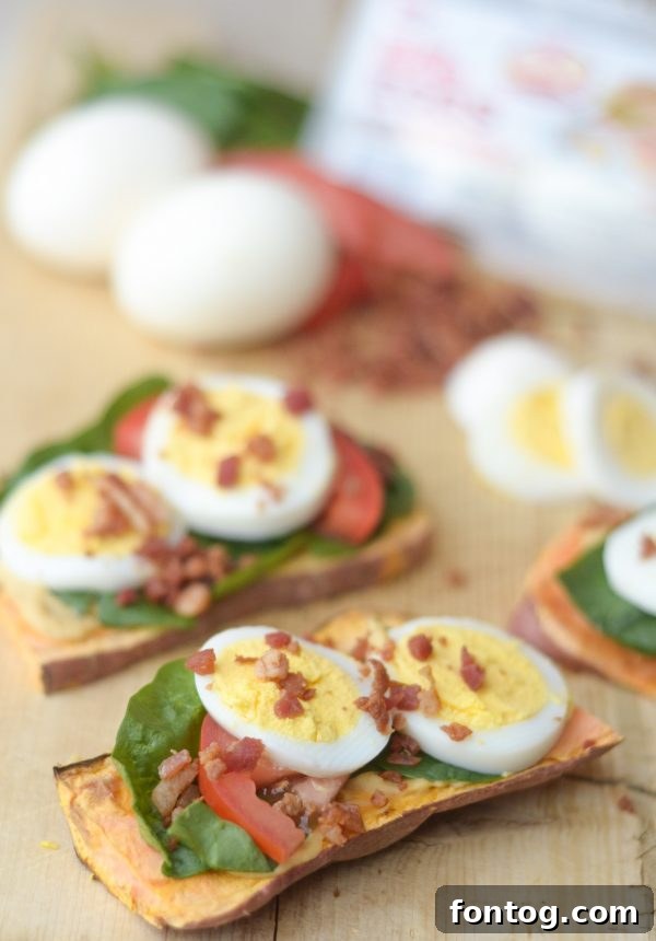Egg Topped Sweet Potato Toast: A vibrant sweet potato slice topped with a perfectly sliced hard-boiled egg, fresh spinach, and a sprinkle of bacon.