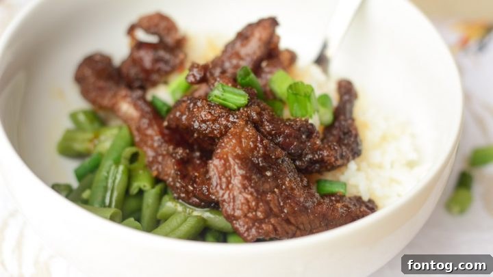 Crispy and flavorful Gluten-Free Air Fryer Mongolian Beef, artfully plated with fluffy white rice and a sprinkle of green onions.
