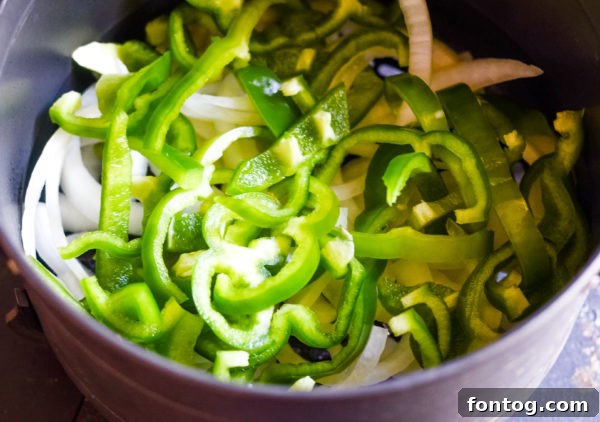 Air Fryer Beer Brat sliced open in a bun, topped with grilled onions and peppers