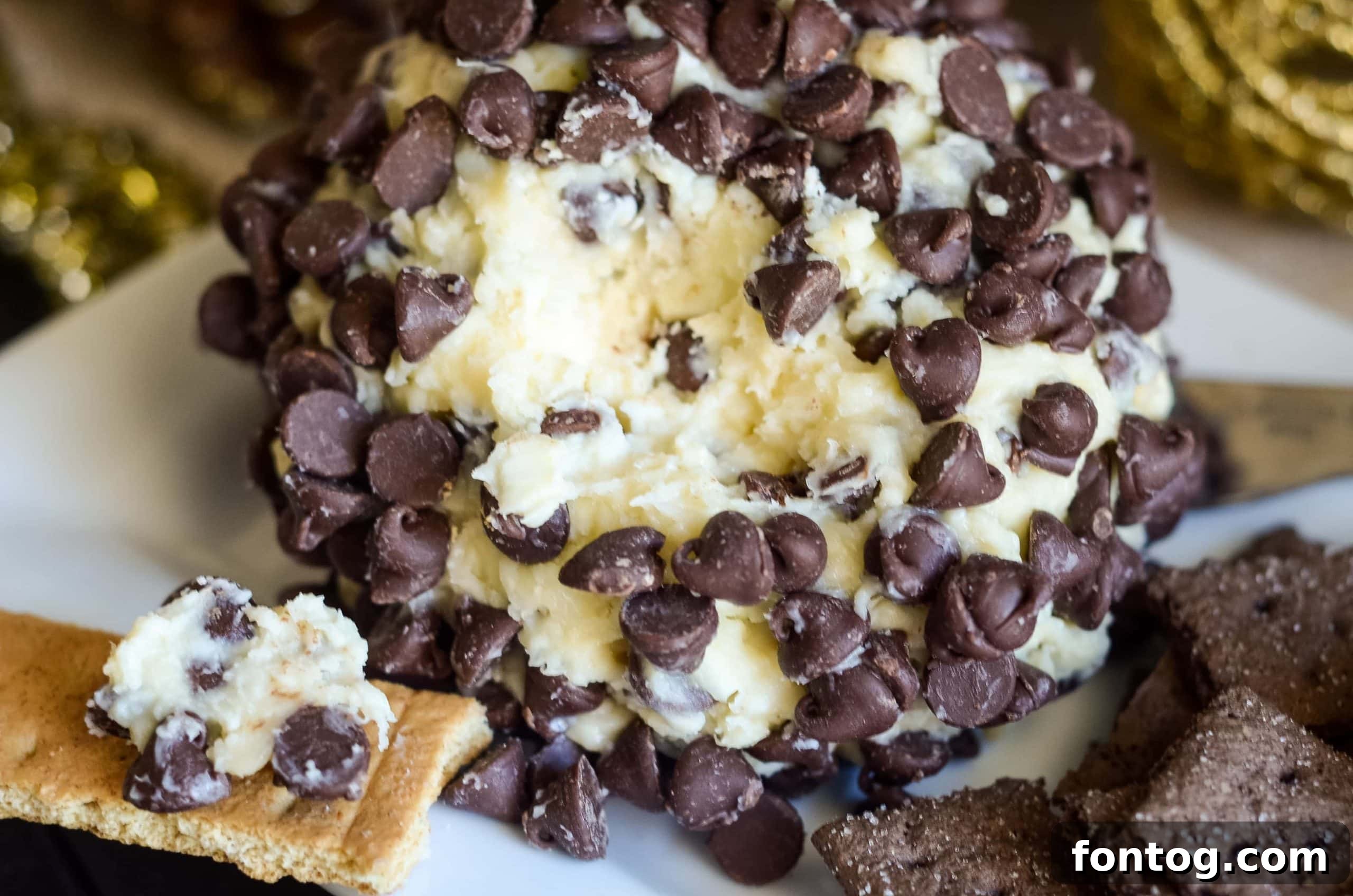 A festive chocolate chip cheesecake ball, surrounded by cookies for dipping.