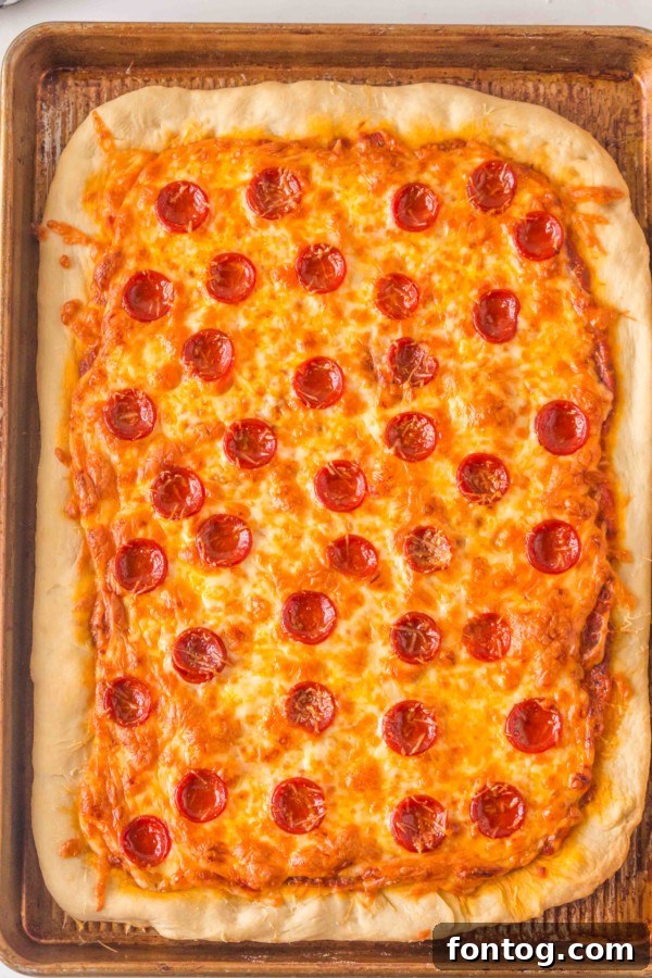 Hands spreading pizza sauce on the rolled-out dough on a sheet pan.